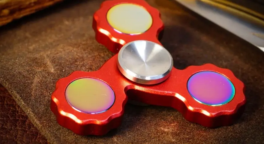 Röd fidget spinner med regnbågseffekter på de tre yttre delarna.