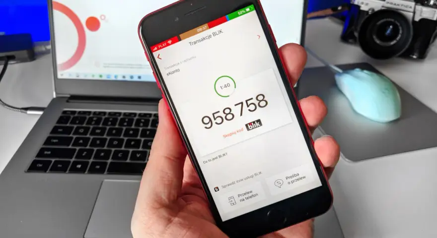 Dłoń trzyma smartfon z aplikacją Blik, na ekranie widoczny kod transakcji.
