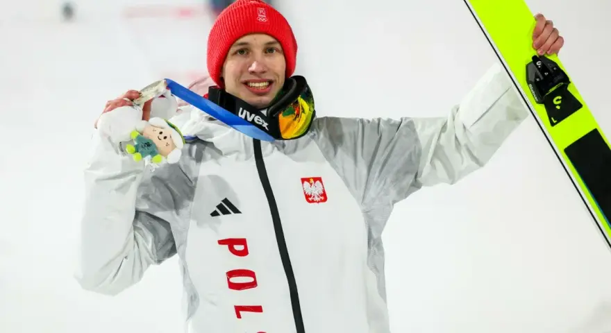 Kacper Tomasiak, skoczek narciarski, z dumą prezentuje medal i narty.