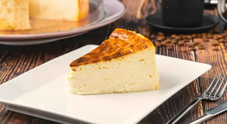 Rebanada de tarta italiana mascarpone con corteza dorada, servida en plato blanco con cubiertos.