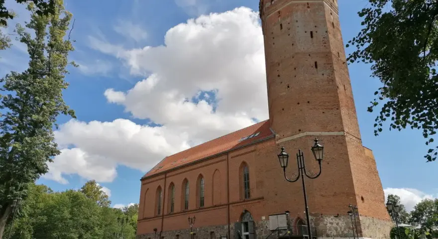 Zamek Człuchów, ceglana wieża i budynek muzeum pod błękitnym niebem z chmurami.