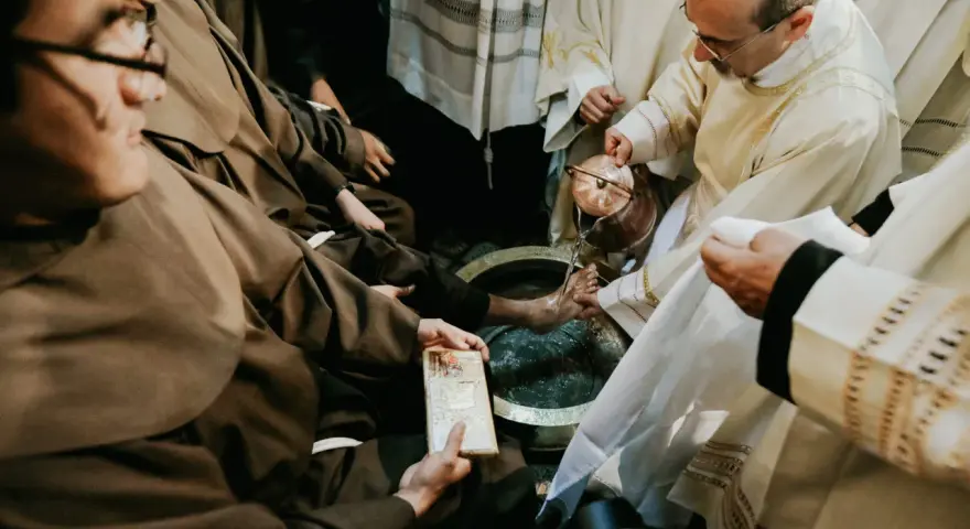During a holy Thursday Catholic homily, a priest washes the feet of a man in a basin, symbolizing Christ's humility.