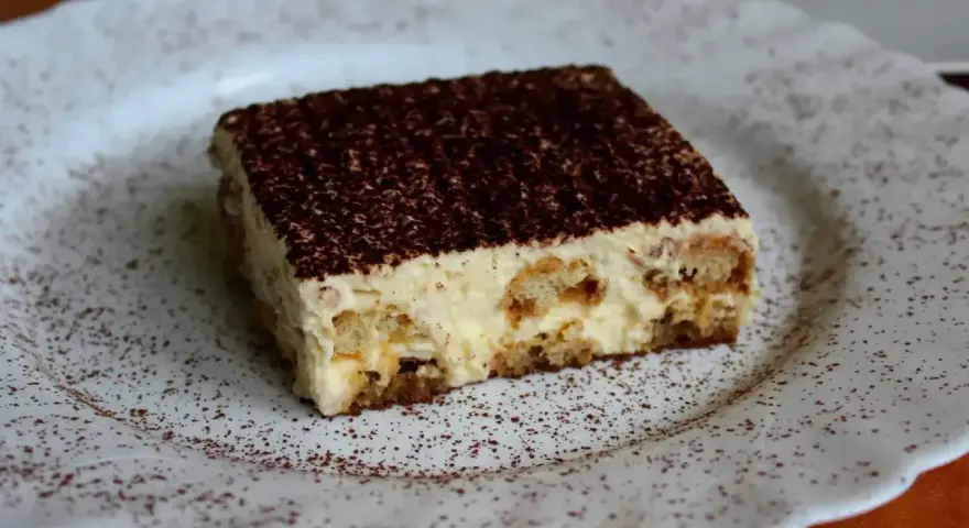 Pyszne tiramisu, czyli zabajone, na białym talerzu, posypane kakao.