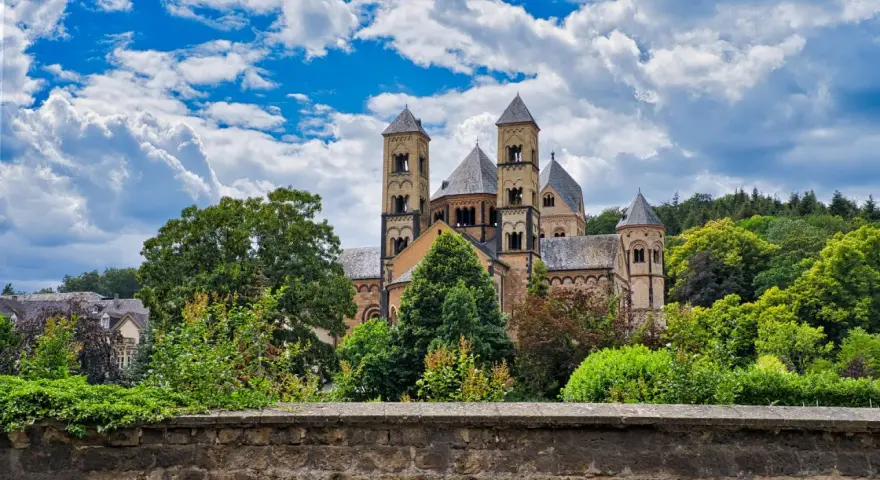 A grand Romanesque abbey, where Benedictine monks lived, stands amidst lush greenery under a dramatic sky.
