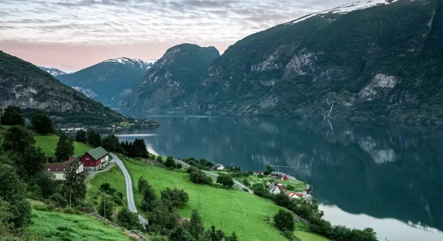 Grönskande bergssluttningar med hus vid en fjord i Norge. Perfekt för att planera dina inreseregler Norge.