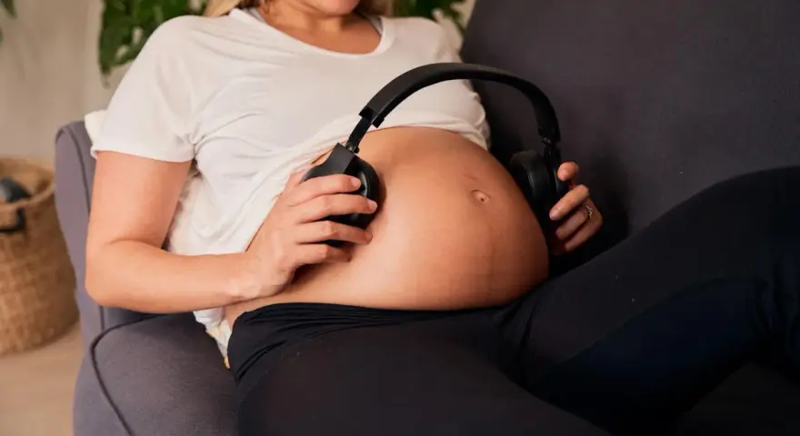 Kobieta w 16 tygodniu ciąży, czyli w 4. miesiącu, przykłada słuchawki do brzucha.