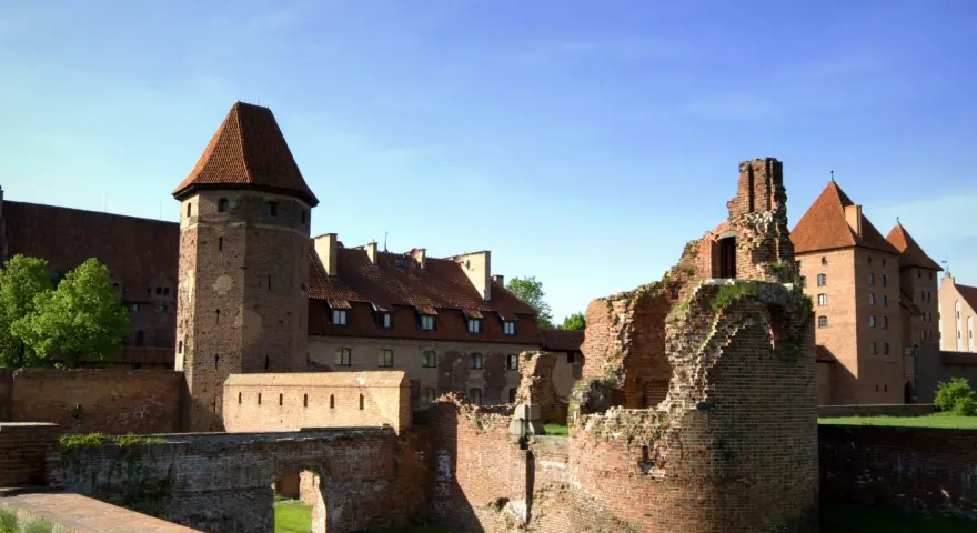 Potężne zamki nad morzem bałtyckim, w tym ruiny i zachowane budowle z cegły, pod błękitnym niebem.