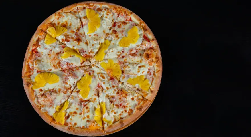 Pizza hawajska z kurczakiem i ananasem na czarnym tle.