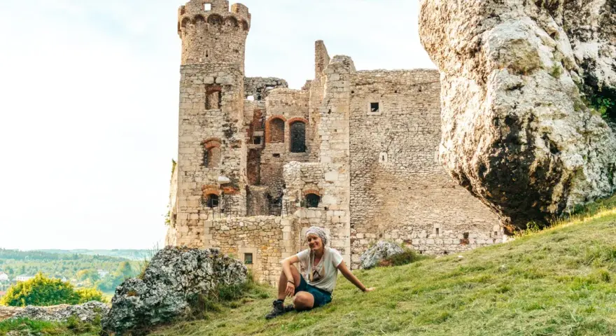 Kobieta odpoczywa na trawie przed ruinami zamku na Szlaku Orlich Gniazd. Ile zamków czeka na odkrycie?