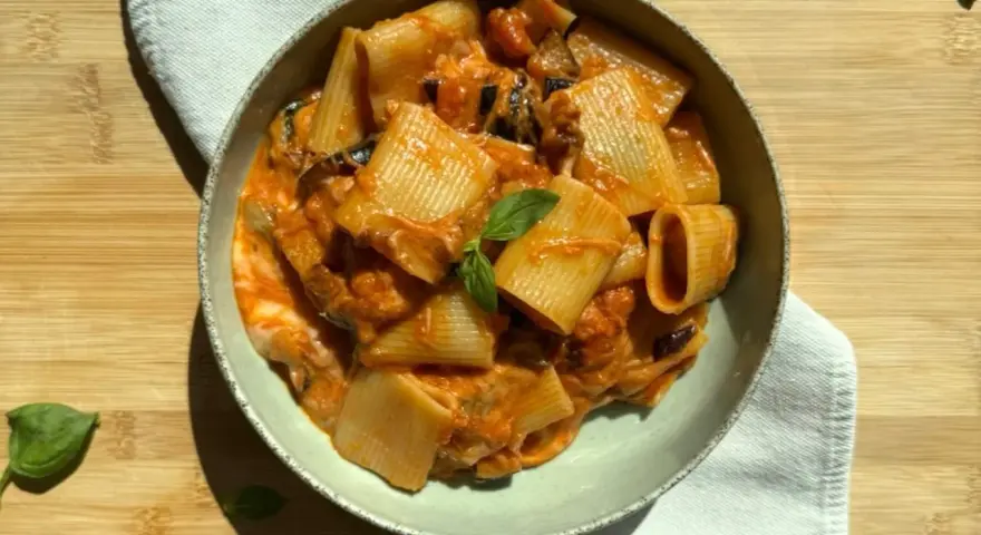 Piatto di pasta alla siciliana con rigatoni, melanzane e pomodoro, guarnito con basilico fresco.