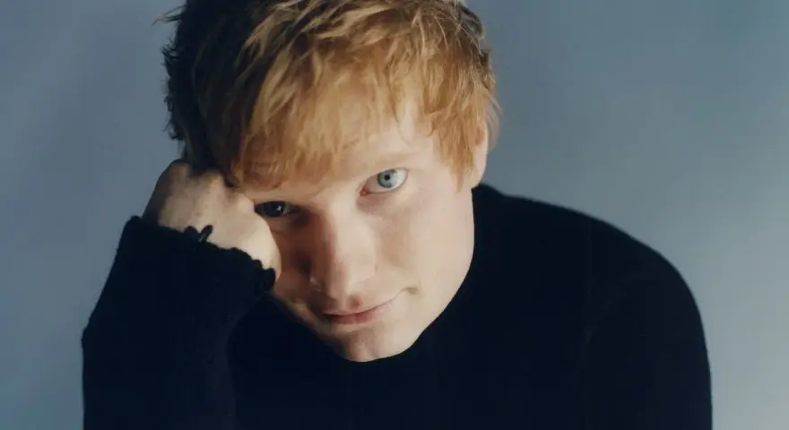 Ed Sheeran w czarnym golfie, opierający głowę na dłoni.