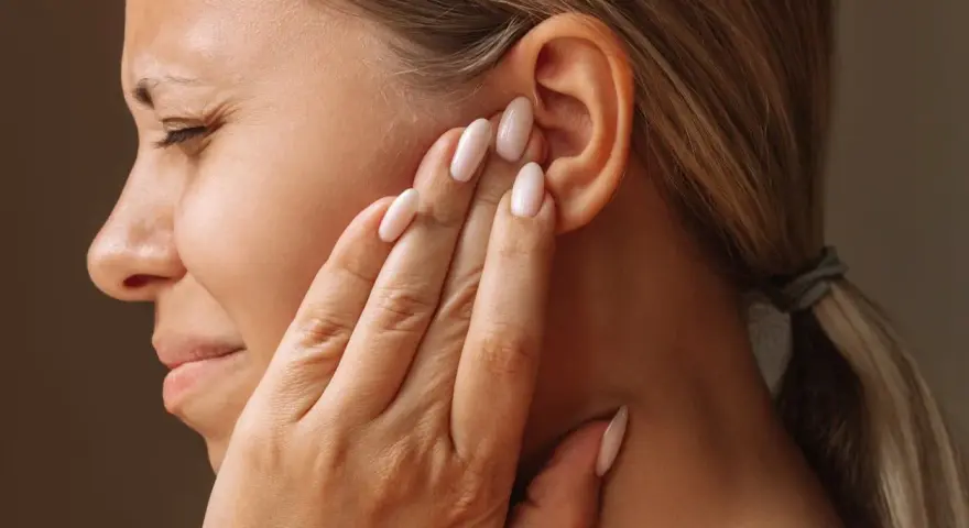 Une femme se tient l'oreille, le visage crispé, comme si elle entendait un bruit sourd dans les oreilles.