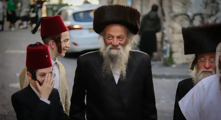 Men in traditional attire, including fur hats and red fez hats, walk together, perhaps celebrating the Purim meaning of joy and community.