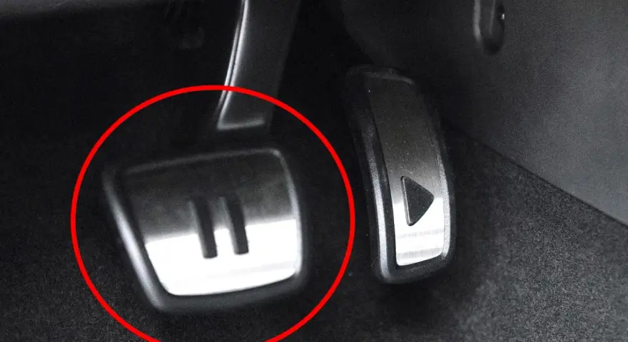 Metalowe pedały w samochodzie, jeden z symbolem "II" (auto hold) i drugi z trójkątem.