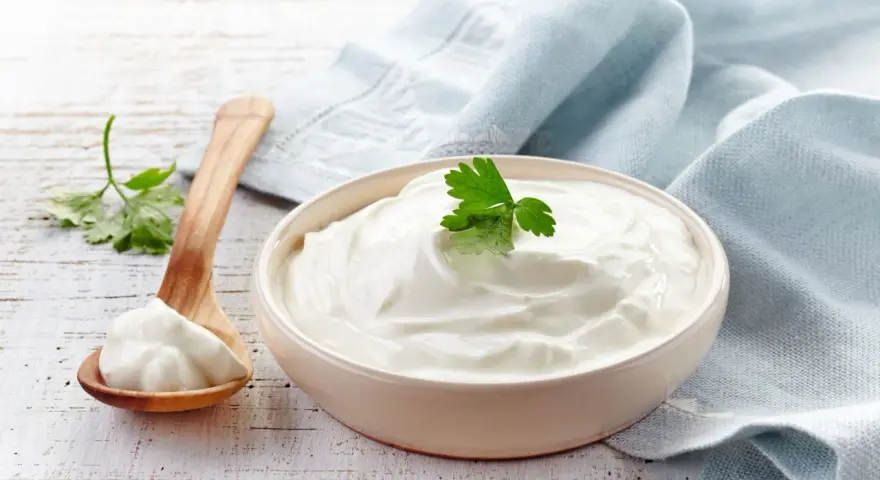 Gęsta, biała śmietana 30 kcal w miseczce, obok drewniana łyżka z porcją. Idealna do deserów i sosów.