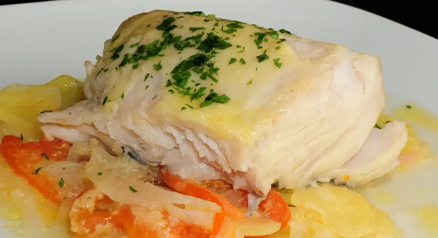 Cogote de merluza jugoso y tierno, servido sobre patatas y tomate, con un toque de perejil fresco.