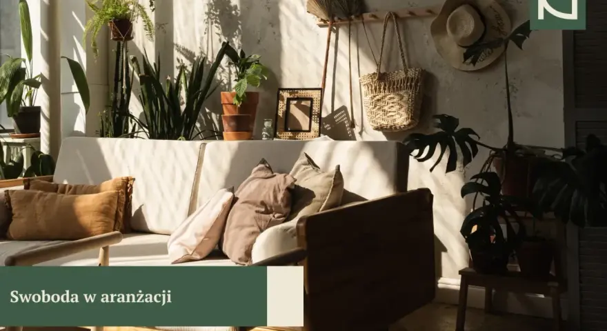 Słoneczny styl boho salonu z mnóstwem roślin, plecionym koszem i słomkowym kapeluszem na ścianie.