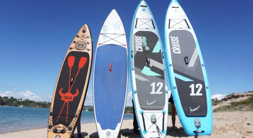 Vier Stand Up Paddles am Strand. Die Boards zeigen verschiedene Designs und Größen, die die Vor- und Nachteile von Stand up paddling beeinflussen können.