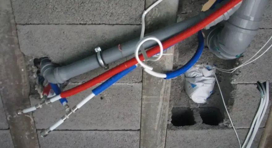 Instalacja wodna z rurami PP w ścianie z pustaków. Widoczne rury czerwone i niebieskie, szary odpływ.