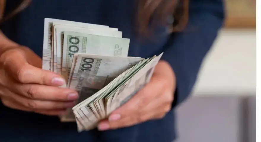 Dłonie trzymające plik polskich banknotów 100 zł. Zastanawiasz się, urlop wychowawczy ile płatny?