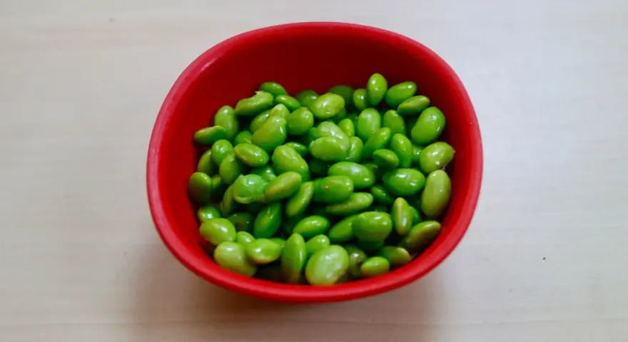 Czerwona miseczka pełna zielonych ziaren soi. Czy to edamame? Tak, to właśnie edamame, zdrowe i pyszne!