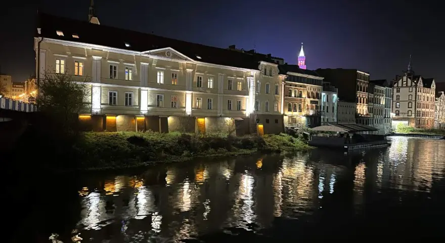 Nocna panorama miasta nad rzeką, z oświetlonymi kamienicami i odbiciami świateł w wodzie. To prawdziwa opolska wenecja.