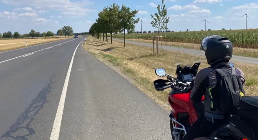 Motociclista su strada panoramica Foresta Nera, con campi di mais e pale eoliche all'orizzonte.
