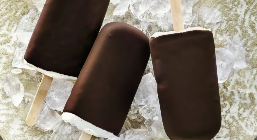 Drei Schokoladen-Vanilleeis am Stiel liegen auf Eiswürfeln.