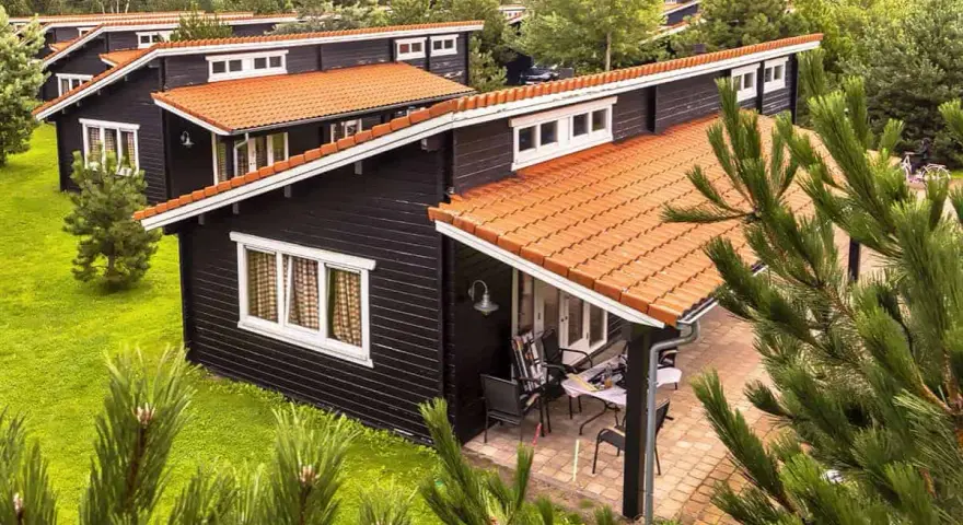 Czarny bungalow z pomarańczowym dachem, otoczony zielenią. To idealne miejsce na wypoczynek, co to znaczy bungalow?