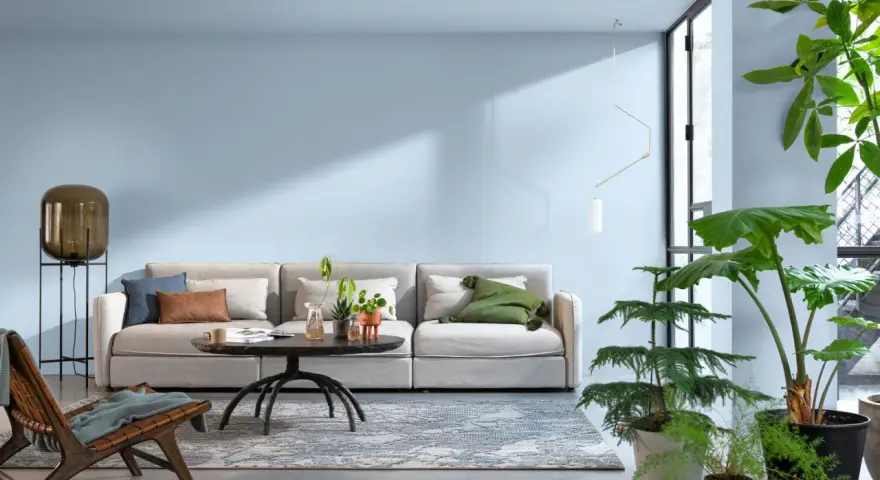 Jasny salon z wygodną kanapą, stolikiem kawowym i dużą ilością roślin. Sufit w kolorze ścian tworzy spójną, spokojną atmosferę.
