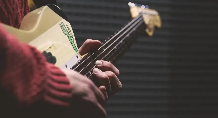 Dłonie grają na gitarze, ludowy instrument szarpany z rysunkiem kaktusa.