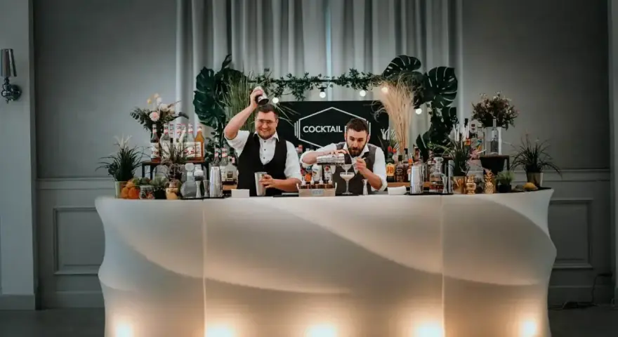 Dwóch barmanów przygotowuje drinki przy nowoczesnym, podświetlanym barze. To idealny drink bar na wesele, oferujący orzeźwiające napoje.