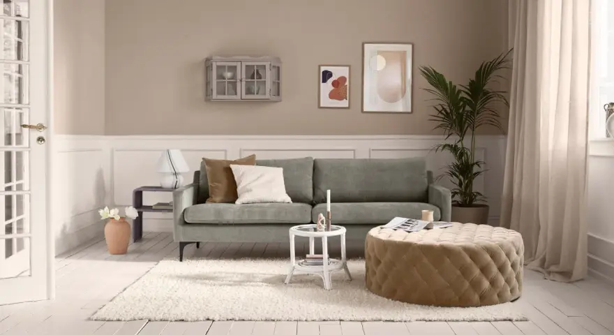 Gemütliches kleines Wohnzimmer einrichten mit grauem Sofa, beigem Hocker, weißem Teppich und Wanddeko.