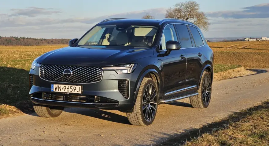Ciemnoszary Volvo XC90 T8 na tle jesiennego krajobrazu. Elegancki SUV z nowoczesnym grillem i światłami LED.