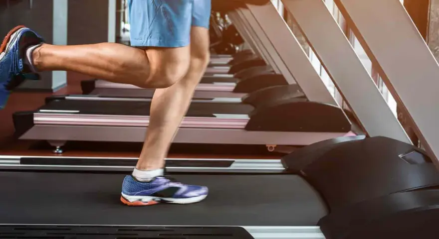 Gambe muscolose in movimento su un tapis roulant, simbolo di corsa indoor e allenamento.