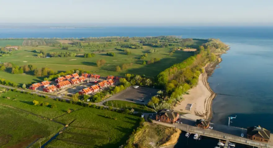 Ferienhäuser am Meer, daneben ein Golfplatz. Ein kleiner Hafen mit Booten.