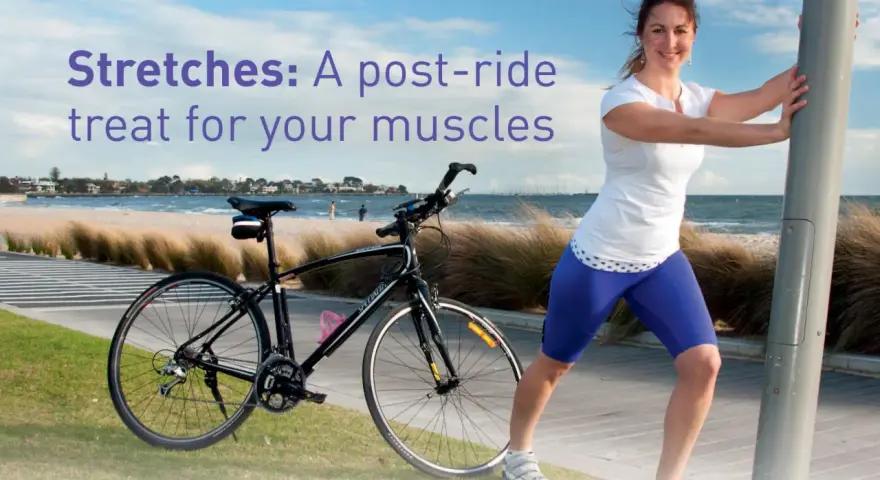 A woman performs a bicycle stretch, leaning on a pole after a ride by the beach.