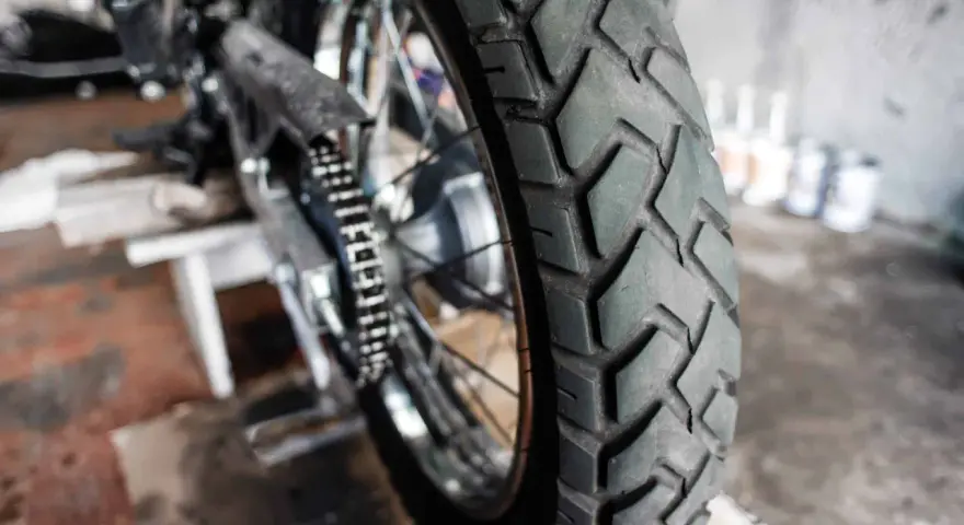 Zbliżenie na bieżnik motocyklowej opony, gotowej do wymiany. W tle widać fragment motocykla i narzędzia.
