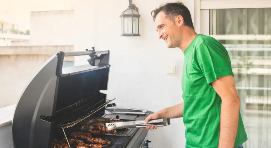 Glad man grillar korv på balkong.