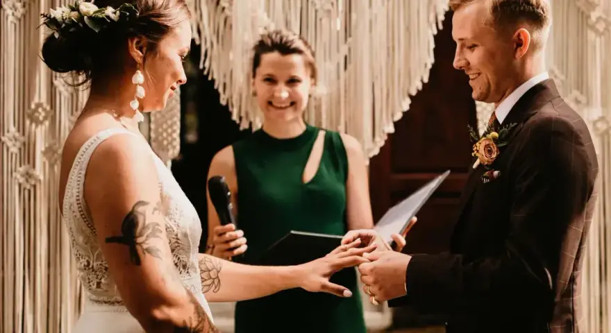 Para ślubuje sobie miłość podczas ceremonii. Panna młoda ma wianek z kwiatów, pan młody garnitur. W tle urzędniczka ślubna. Pytanie: jakie dokumenty do ślubu cywilnego?