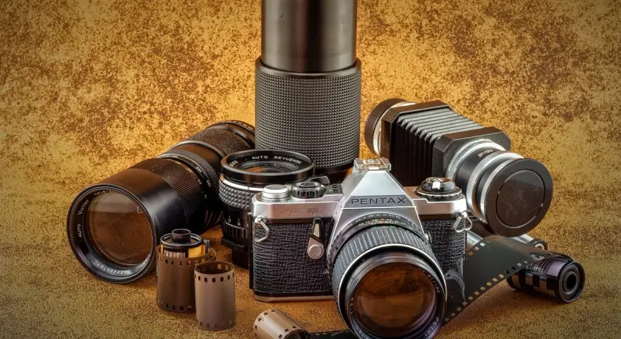 Kolekcja różnych rodzajów aparatów fotograficznych i akcesoriów, w tym aparat Pentax, obiektywy i klisze.