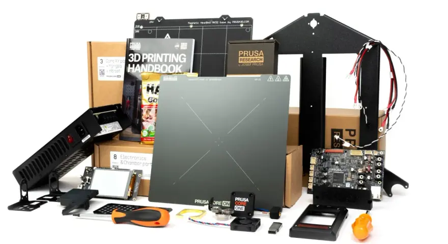 Zestaw części do drukarki 3D Prusa Core One: płyta główna, zasilacz, ekran, instrukcja, elementy konstrukcyjne i akcesoria.
