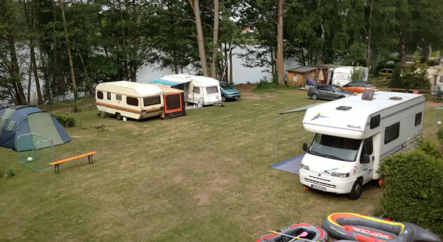 Campingplatz am sonnensee flachslanden mit Wohnmobilen, Wohnwagen, Zelt und Schlauchbooten am Ufer.