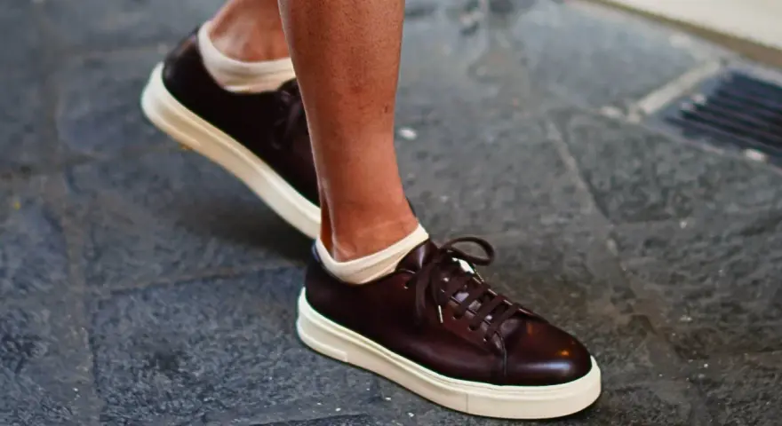 Un uomo indossa sneakers marroni con calze bianche a vista. Un look casual ma curato, perfetto per chi cerca quali calze con sneakers uomo.