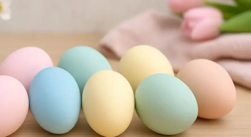 Huevos de pascua para pintar en tonos pastel, listos para decorar. Flores y tela suave al fondo.