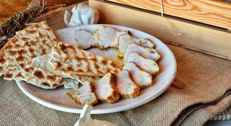 Lomo de orza en rodajas, servido con pan crujiente y ajo. Un plato rústico y delicioso.