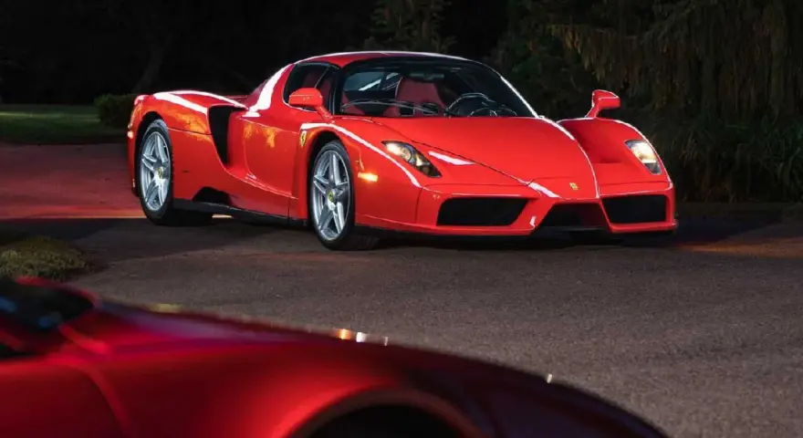 Czerwone Ferrari Enzo zaparkowane nocą na drodze, z innym czerwonym samochodem w tle.