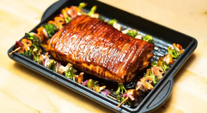 Succulento arrosto di manzo glassato, servito su una teglia con spiedini di verdure miste, tra cui broccoli e cipolle rosse.