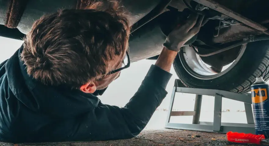 Un giovane impara come si diventa meccanico, lavorando sotto un'auto con attrezzi e spray.
