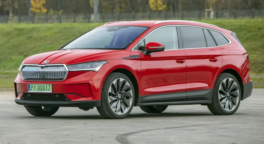 Czerwona Skoda Enyaq na tle zieleni, z tablicą rejestracyjną PY 00017. Ten elektryczny SUV oferuje imponujący zasięg.